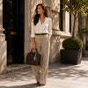 Woman walking outside wearing a white shirt, beige trousers, and holding a Tote Leather Handbag.