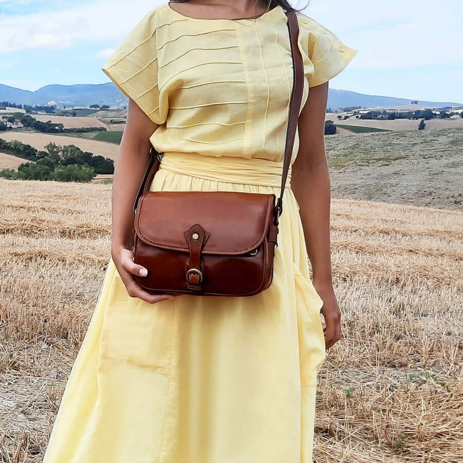 Woman wearing a brown leather shoulder bag across the body in a countryside setting