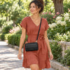 A woman wearing a rust-colored linen dress with short sleeves and a tie waist, carrying the black crossbody phone wallet for Women  walking along a garden path.