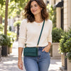 A woman wearing a cream ribbed knit sweater and blue jeans walks outdoors carrying the Teal Crossbody Phone Wallet For Women 