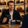 Man showing Mens Bifold Wallet With ID Window at a leather goods store, showcasing card slots and ID window.
