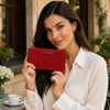 Woman holding a red Ladies Leather Zip Around Wallet in an elegant outdoor setting.