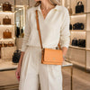 A woman wearing a white sweater and beige pants, showcasing a Genuine Leather Shoulder Bag in a boutique setting.