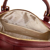 Close-up of the interior of a bordeaux Italian leather duffle bag, showing a beige patterned lining, open pocket and gold-tone hardware.