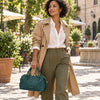 Elegant woman in a trench coat holding the Italian Leather Duffle Bag in green.