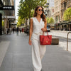 Woman walking in city wearing white outfit and sunglasses, carrying a red Italian Handbag.
