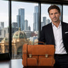 Man in a suit holding a Ventimiglia Italian Leather Briefcase in a city office setting.