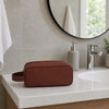 The Brown Italian Leather Toiletry Bag sitting on the bathroom sink