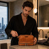 Man in a robe using the Mens Toiletry Bag Leather in a modern bathroom setting.