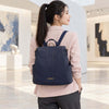 A woman wearing a light pink blazer and dark gray pants is shown from behind, carrying The Dark Blue Ladies Backpack with gold-tone hardware in a modern art gallery setting.