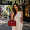 Stylish woman holding a red Ladies Duffle Bag on Bourke Street, showcasing urban elegance and practicality.