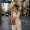 Woman in beige jumpsuit carrying a tobac Ladies Duffle Bag on Swanston Street.
