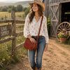 Woman in a white blouse and cowboy hat holding an Ladies Leather Bag, posing on a rustic farm path.