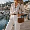 Woman wearing a light shirt and white pants holding a Leather Clutch Bag for Women near a marina.