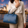 Elegant woman holding a denim Ladies Leather Duffle Bag in front of a scenic city backdrop.