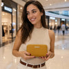 A stylish woman holding a Ladies Purse in mustard while smiling in a mall setting.