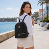 Young woman in casual attire wearing a Ladies Small Leather Backpack by the waterfront.