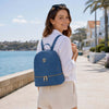 A woman wearing a Ladies Small Leather Backpack in blue by the waterfront, showcasing its stylish design and practicality.