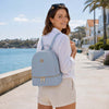 Woman wearing a Ladies Small Leather Backpack in light blue, standing by the water.