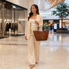 Woman in a stylish suit carrying a Large Italian Handbag while walking in a modern shopping mall.