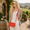 Model wearing a stylish outfit with a coral leather clutch bag in a vineyard setting.