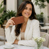 Woman holding a Leather Accordion Wallet in a café, showcasing its sleek design and practicality.