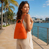 Woman wearing an orange Leather Backpack For Women on a sunny waterfront pathway.