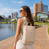 Woman wearing Leather Backpack Ladies near a river with city skyline in the background.