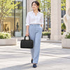 A woman wearing a white shirt and light blue trousers carrying a Italian Leather Bowler Bag while walking outdoors.