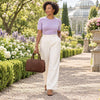 Woman in a garden wearing light purple top and white pants, carrying an Italian Leather Bowler Bag.