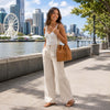 Woman in a white tank top and beige pants carrying a leather bucket bag by the river in the city.