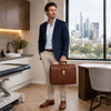 A man in a navy blazer holding a brown Leather Doctor Bag in a modern office setting with city skyline views.