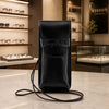 Leather Eyeglasses Case in black leather with shoulder strap on display in a stylish store.