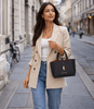 A woman wearing a beige blazer holds the Leather Handbag in a black color while walking down a city street.