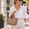 A woman wearing a white shirt holds the Leather Handbag in a caramel color while walking down a city street.