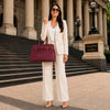 A stylish woman wearing a suit, holding a Leather Womens Handbag outside Parliament of Victoria.