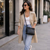 A woman walking on a city sidewalk carrying a black leather ladies handbag