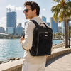 Man wearing a leather laptop backpack by the waterfront, showcasing stylish design and functionality.