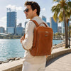 Man wearing a Leather Laptop Backpack near a waterfront in a city.