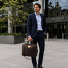 Man in suit holding Luxury Leather Laptop Bag outside a modern building.