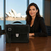 Woman sitting at a table with Leather Laptop Briefcase against a waterfront backdrop.