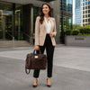 A professional woman in a beige blazer and white shirt holding a Leather Business Laptop Bag outside in a city environment.