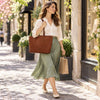 Woman walking in a stylish outfit carrying a Leather Shopping Tote Bag on a sunny street.