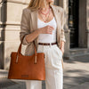 Fashionable woman wearing a beige blazer, showcasing an elegant brown Leather Tote Bag on the street.