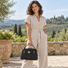 Woman wearing a linen jumpsuit holding a Leather Tote, surrounded by a scenic Italian landscape.