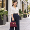Elegant woman in a white shirt and dark pants holding a Bordeaux Leather Tote in a stylish city setting.