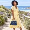 Woman in a yellow dress holding Leather Tote near a scenic beach.