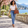 Woman walking by the lake wearing a white blouse and jeans, carrying a Leather Tote Handbag.