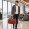 Elegant man carrying a Leather Travel Bag at an airport, showcasing luxury travel style.