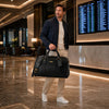 Man holding a Leather Travel Bag Small in a modern hotel lobby.